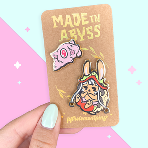 made in abyss gold hard enamel pins nanachi and mitty on a kraft backing card with golden foil "made in abyss" written across the top with gold foil logo on bottom